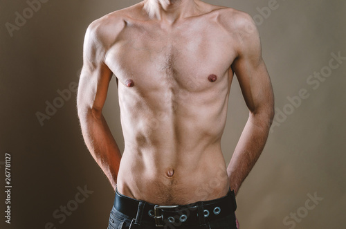 Naked torso of a young, slim, pumped-up man on a beige background. Tight naked attractive man in black jeans.
