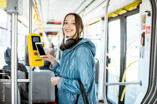 Portarit of a young smiling woman paying conctactless with smartphone for the public transport in the tram