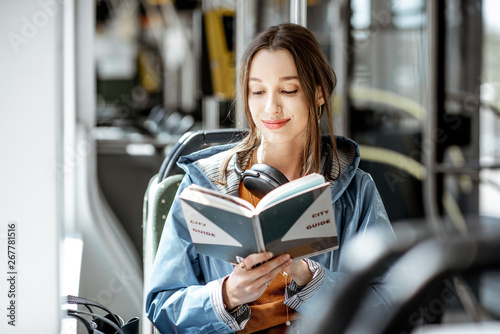 Tableau sur toile Young woman reading book while moving in the modern tram, happy passenger at the