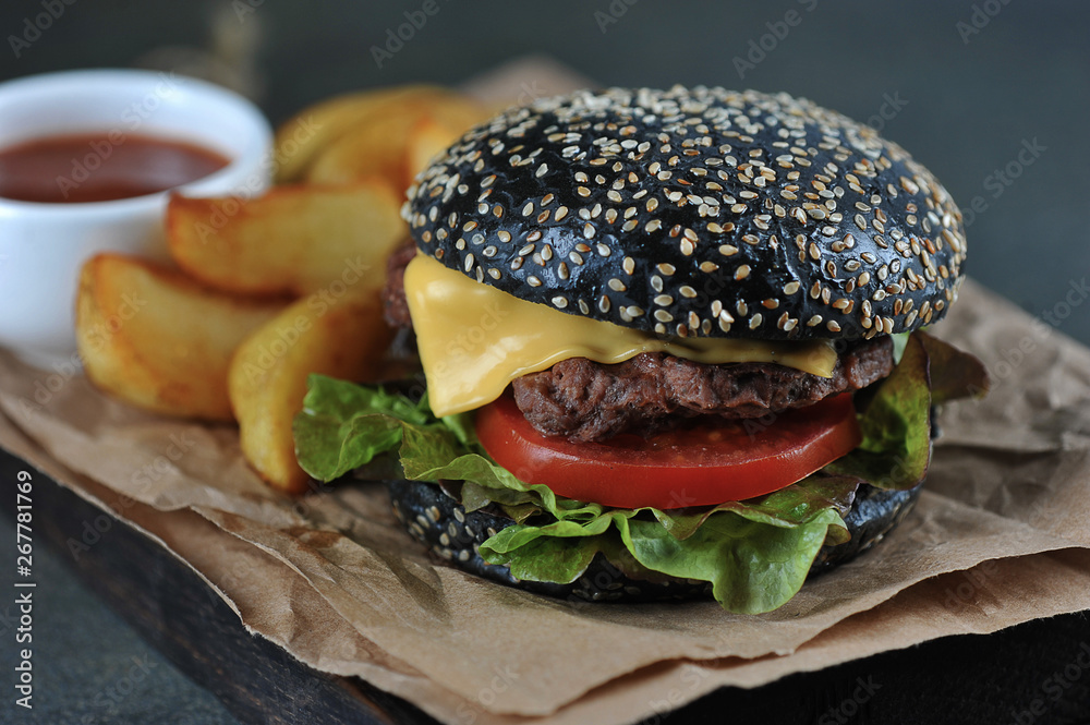 Black burger with cheese, lettuce, beef patty, slice of tomato. Idaho potatoes and Sauce