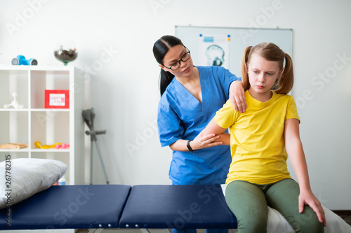Uncomfortable young girl allowing dark-haired nurse moving her hand