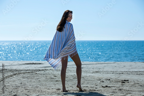 Pretty young girl wrapped in beach towel poses to camera. Full length photo shoot and wonderful hair. Healthy, beauty and summer holiday concept.