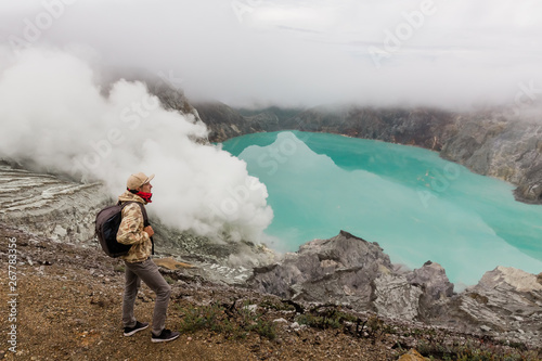 Man tourist looks at the sulphur lake on the Ijen volcano on the island Java in Indonesia. Hiker man with backpack travel on top mountain, travel concept