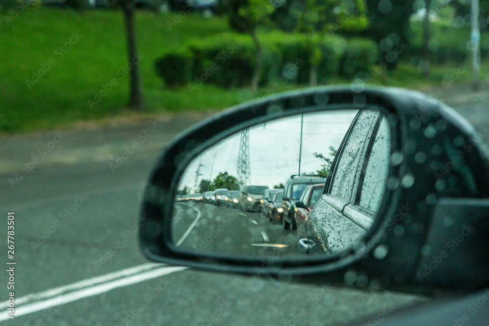 a side mirror of a car in rainy weather and traffic jams. in focus raindrops of the car.