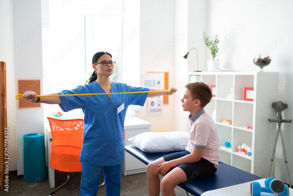 Fototapeta premium Serious hard-working young man spreading yellow resistance band