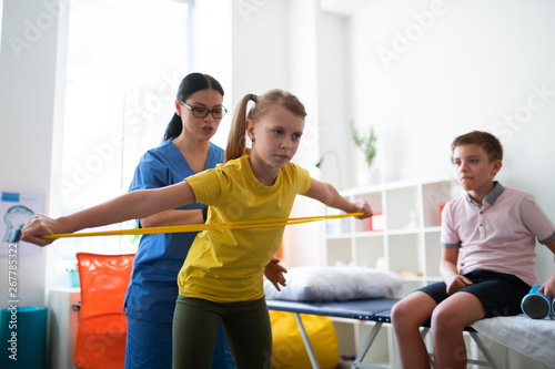 Fotografie Attentive long-haired Asian therapist changing posture of little girl