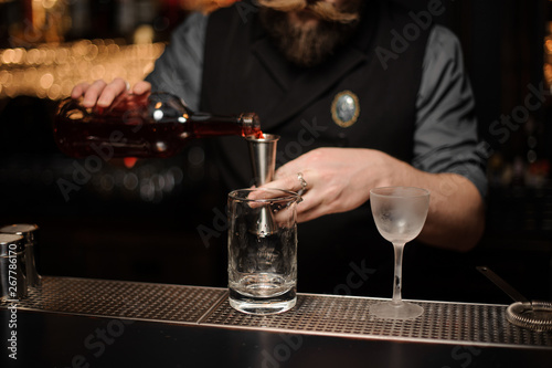 Male bartender pours alcohol drink with jigger