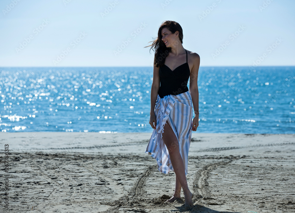 Pretty young girl wrapped in beach towel posing to the camera. Full length photo shoot and wonderful hair. Healthy, beauty and summer holiday concept.