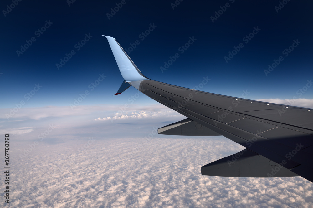 Obraz premium Jet aircraft wing flying above clouds with blue sky