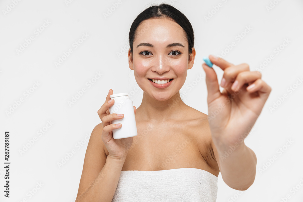 Pretty asian woman with healthy skin posing naked isolated over white wall background holding vitamins pill.