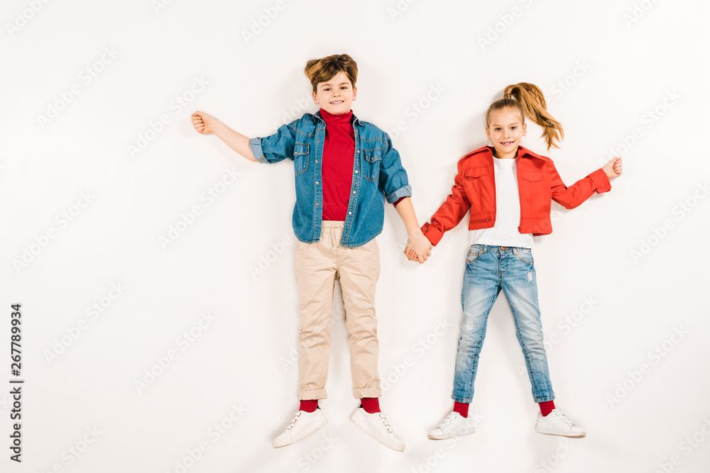 cheerful kids holding hands and smiling while lying on white cheerful kids holding hands and smiling while lying on white