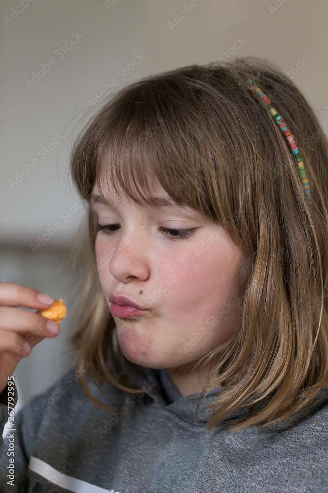 Vertical closeup of pretty fair pre-teen girl pouting while staring at a piece of flavoured popcorn Vertical closeup of pretty fair pre-teen girl pouting while staring at a piece of flavoured popcorn
