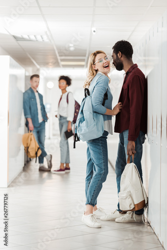 full length view of smiling multiethnic students standing in corridor in college