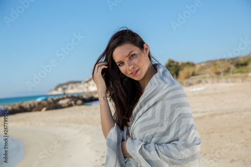 Pretty young girl wrapped in beach towel poses on camera with a smiling face. Portrait shot and wonderful hair. Beauty and summer concept. 