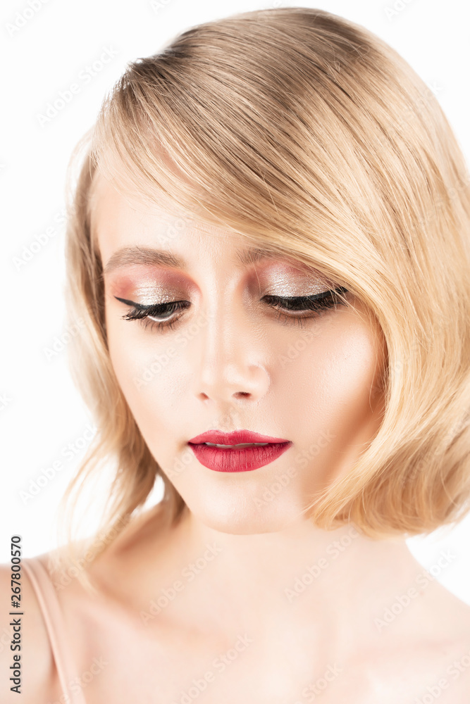 Cute blond girl with big beautiful eyes, red lips and vintage style hairstyle, wearing a golden sparkling dress looks down. Isolated on white. Clean, healthy skin