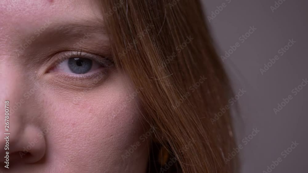 Half face shot of young female student watching seriously and peacefully into camera on gray background. Half face shot of young female student watching seriously and peacefully into camera on gray background.
