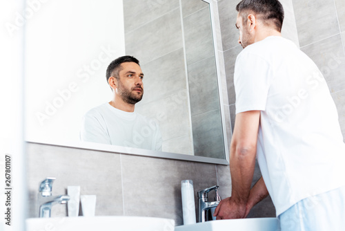 handsome man looking in mirror and washing hands in bathroom during morning routine