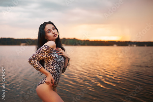 Sexy brunette woman. Young female relaxing on the beach during sunset. Perfect body girl with wet clothes and hair posing provocatively in summer evening at beach. photo