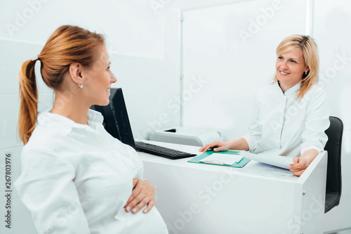 Smiling obstetrician talking with pregnant woman in clinic examination room. Consultation pregnancy