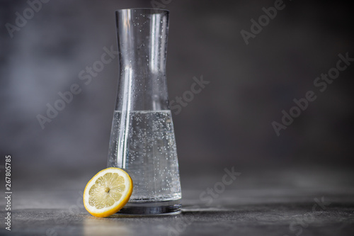 Karafka z woda gazowaną, siwe tło oraz cytryna © skora-fotoprojekt