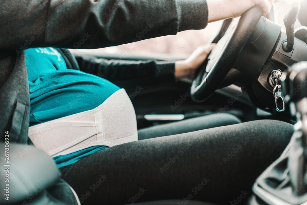 Close up of pregnant woman driving car. Hands on steering wheel.