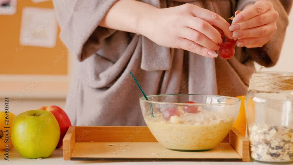 Healthy detox breakfast. Woman in bathrobe adding grapes corn balls to muesli stirring. Glass of orange juice on tray. Healthy detox breakfast. Woman in bathrobe adding grapes corn balls to muesli stirring. Glass of orange juice on tray.