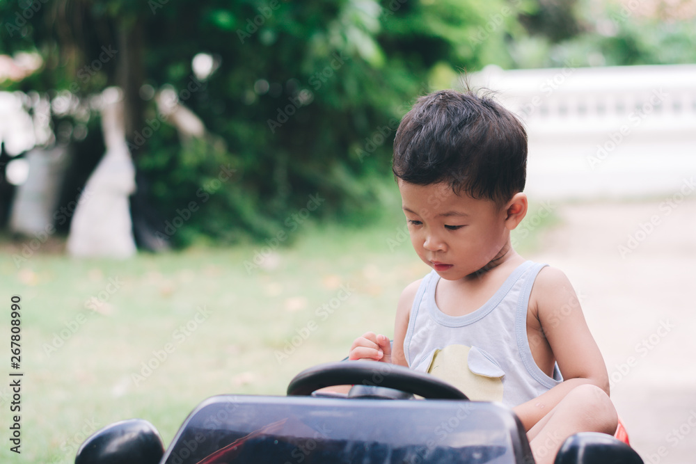 Little boy driving red car with the steering wheel. Little boy driving big toy car and having fun on grass outdoors. Little boy driving red car with the steering wheel. Little boy driving big toy car and having fun on grass outdoors.