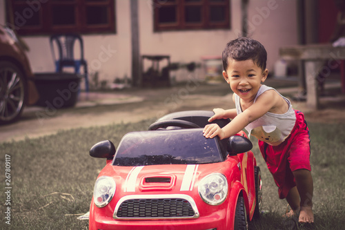 Little boy driving red car with the steering wheel. Little boy driving big toy car and having fun on grass outdoors.