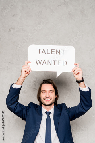 cheerful recruiter holding speech bubble with talent wanted lettering on grey