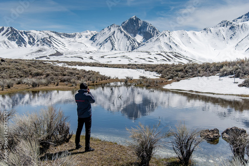 Asian man tourist and photographer holding DSLR camera taking photo of Mammoth mountain landscape from the lake in Hot Creek Geological Site in winter. Travel photography concept