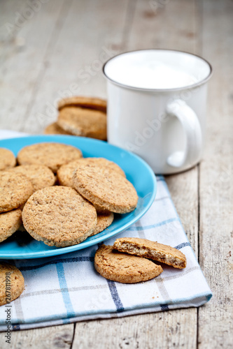 Fresh baked oat cookies on blue ceramic plate on linen napkin and cup of milk