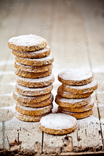 Fresh oat cookies stacks with sugar powder closeup on rustic wooden table.