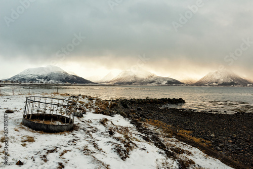 old floating basket unused, placed on the  black rocks beach With a snow-covered mountain in the back In the morning, the cloudy day and the sun shone down to hit the sea and mountains