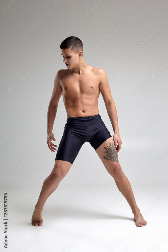 Photo of a handsome man ballet dancer, dressed in a black shorts, making a dance element against a gray background in studio.