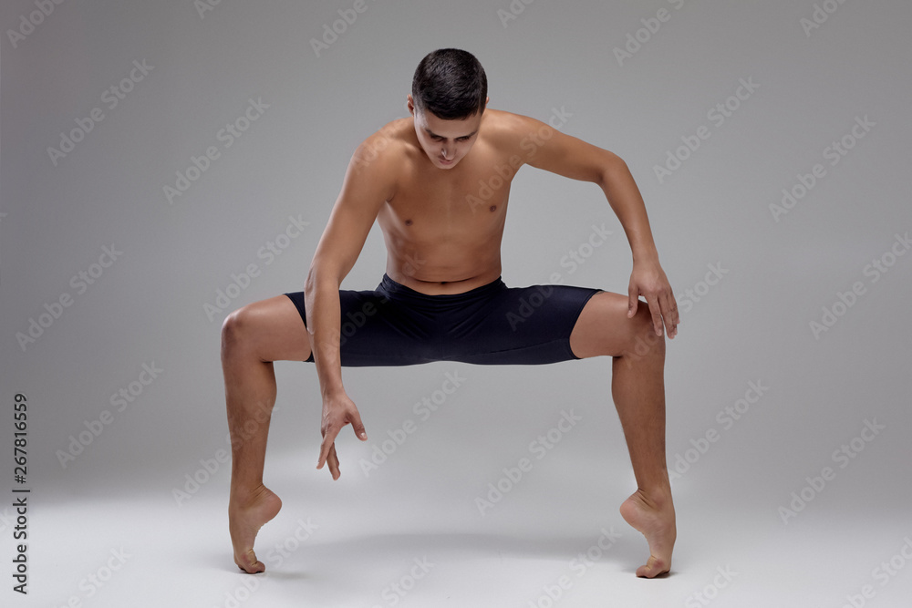 Photo of a handsome man ballet dancer, dressed in a black shorts, making a dance element against a gray background in studio. Photo of a handsome man ballet dancer, dressed in a black shorts, making a dance element against a gray background in studio.