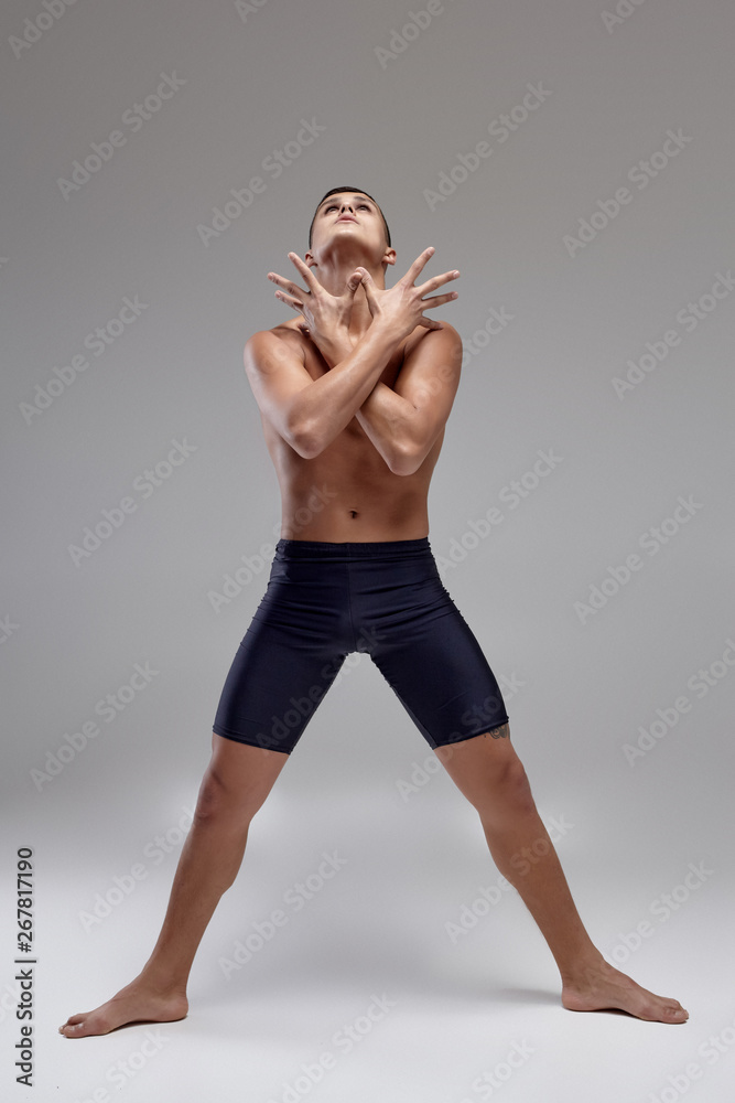 Photo of a handsome man ballet dancer, dressed in a black shorts, making a dance element against a gray background in studio. Photo of a handsome man ballet dancer, dressed in a black shorts, making a dance element against a gray background in studio.