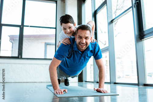 happy father doing push up exercise with son on back at gym
