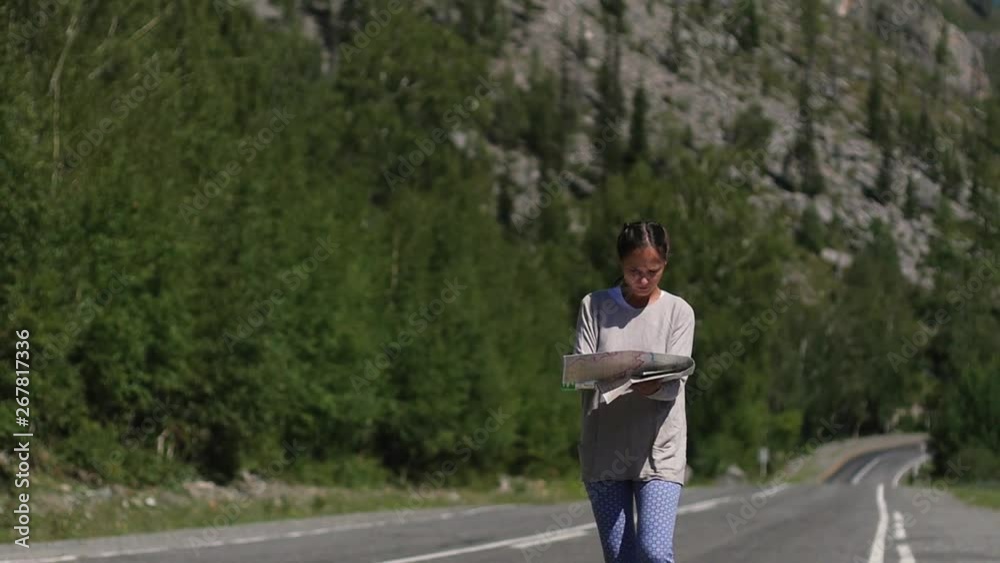 Young woman tourist with a map in hand goes on the road. female traveler is looking for her way. a woman walks along the road and holds a map in her hands against the backdrop of a mountain landscape Young woman tourist with a map in hand goes on the road. female traveler is looking for her way. a woman walks along the road and holds a map in her hands against the backdrop of a mountain landscape