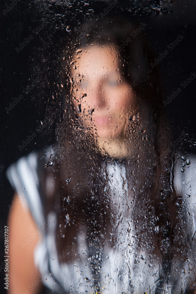 Chica joven, vista a través de un espejo lleno de gostas agua