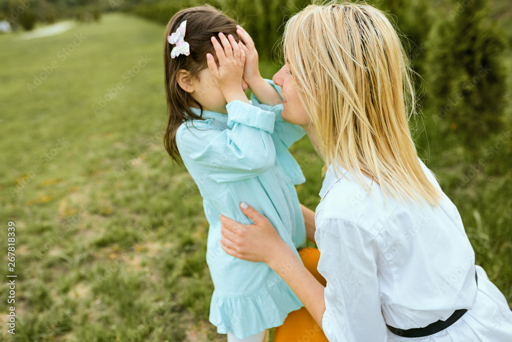 Pretty kid playing hide-and-seek with young mother outdoor. Portrait of joyful woman and her cute child playing in the park. Mother and daughter shares love. Happy Mothers Day. Motherhood, childhood Pretty kid playing hide-and-seek with young mother outdoor. Portrait of joyful woman and her cute child playing in the park. Mother and daughter shares love. Happy Mothers Day. Motherhood, childhood