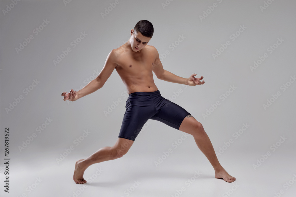 Photo of a handsome man ballet dancer, dressed in a black shorts, making a dance element against a gray background in studio.