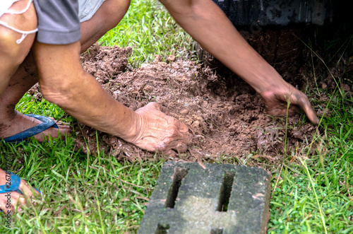 Thailand, February 28, 2562 : The elderly man is using his hand or hoe to dig the soil that is dirty. So that the stuck car can come out. photo