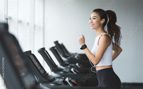 Canvas Print Young woman exercising on treadmill and listening music