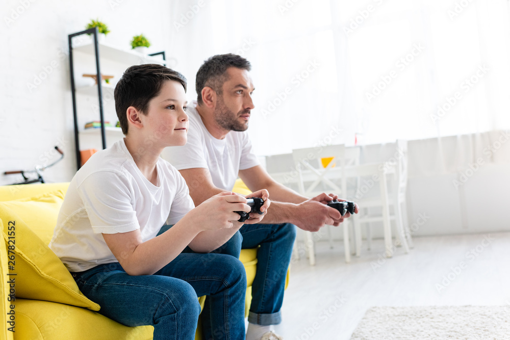 father and son playing Video Game on couch in Living Room with copy space father and son playing Video Game on couch in Living Room with copy space