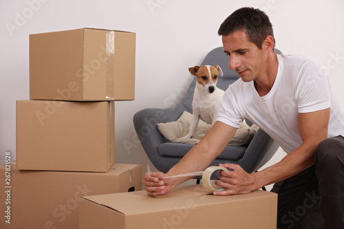 Moving in and out. Man packing boxes with dog watchig. New home concept