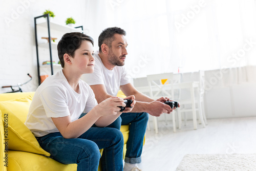 father and son playing Video Game on couch in Living Room with copy space