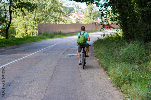 Fototapeta Naklejka Na Ścianę i Meble -  The guy rides a bike on the road in the summer - rear view.