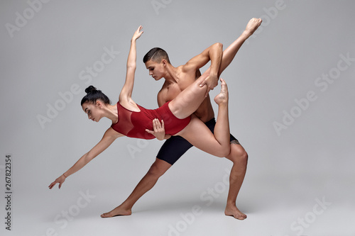 Fototapeta Naklejka Na Ścianę i Meble -  The couple of an athletic modern ballet dancers are posing against a gray studio background.