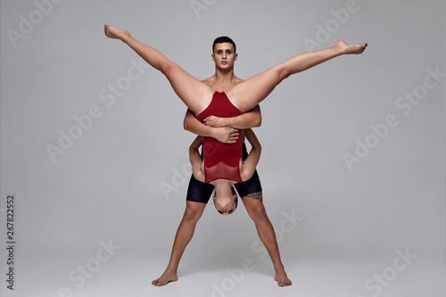 The couple of an athletic modern ballet dancers are posing against a gray studio background.
