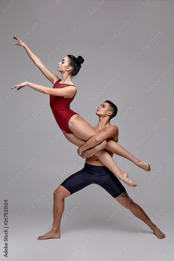 The couple of an athletic modern ballet dancers are posing against a gray studio background.